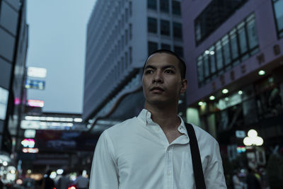 Portrait of young man standing against buildings in city