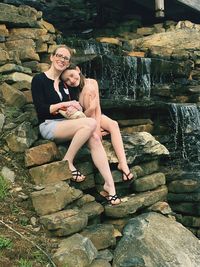 Portrait of smiling woman with daughter sitting on rocks