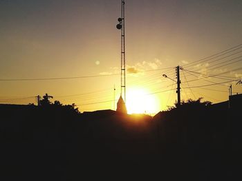 Low angle view of silhouette electricity pylon against orange sky