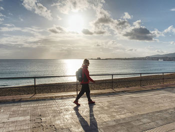 Female backpacker walk or strolling along the beach promenade, sun at horizon