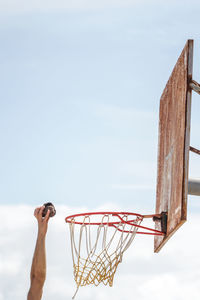 Cropped hand of man throwing equipment in basketball hoop against sky