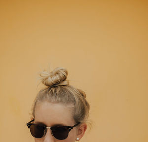 Close-up of young woman with hair bun against yellow background