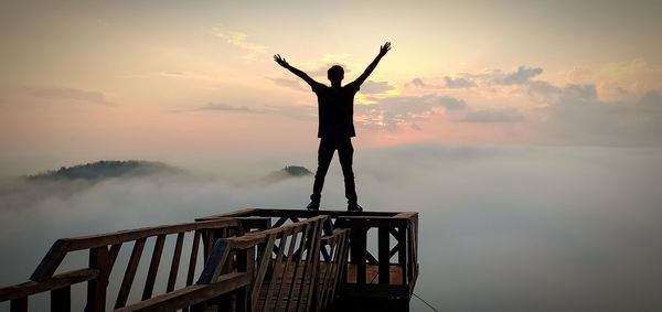 Silhouette man standing by railing against sky during sunset