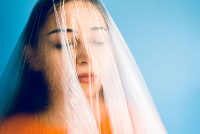 Teenage girl wrapped in plastic against blue background