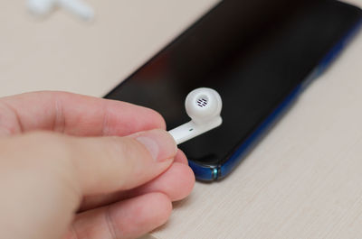 White wireless earphone in hand, music in smartphone