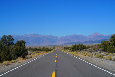 Empty road by mountains against clear blue sky