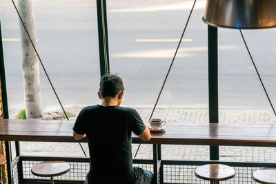 Rear view of boy sitting on table by window