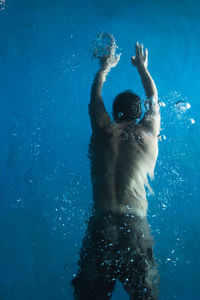 Rear view of shirtless man swimming in pool