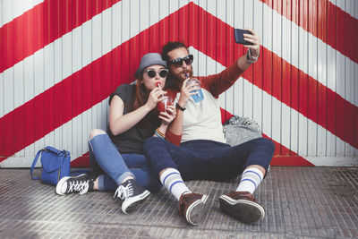 Young couple with soft drinks taking selfie with smartphone