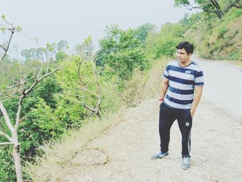 Full length of young man standing by road against sky