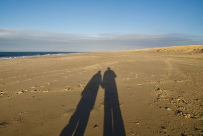 Shadow of people on sand at beach against sky