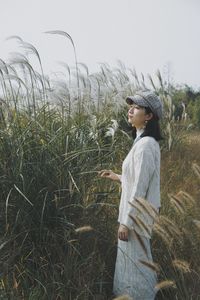 Side view of young woman standing on field against sky