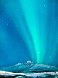 Low angle view of snowcapped mountain with aurora against blue sky at night