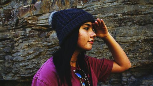 Young woman shielding while looking away against rock formation