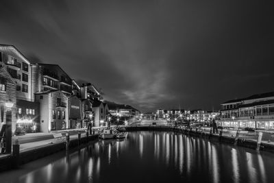 Illuminated buildings by river against sky at night