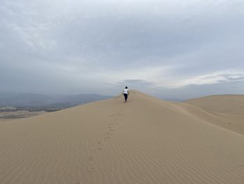 Man on sand dune in desert against sky