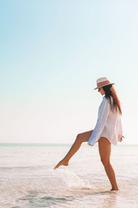 Woman with arms raised on beach against clear sky