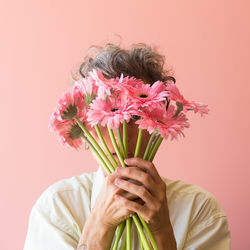 Close-up of hand holding pink flowers against gray background