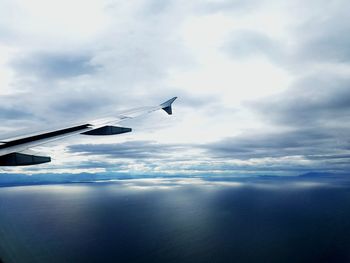 Cropped image of airplane flying over sea against cloudy sky