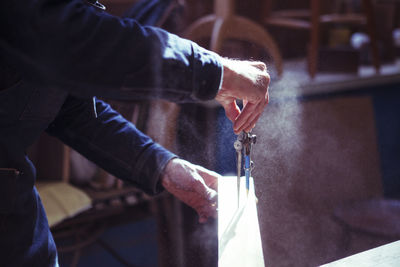 Midsection of carpenter using compass on wooden plank in workshop