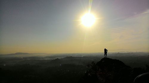 Silhouette man standing on landscape against sky during sunset