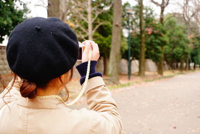 Rear view of woman photographing through camera on road