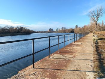 Footpath by railing against blue sky during winter