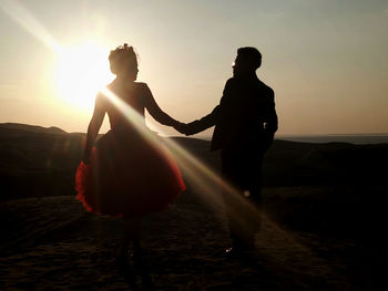 Silhouette couple holding hands against sky during sunset
