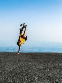 Boy doing handstand on road against clear blue sky