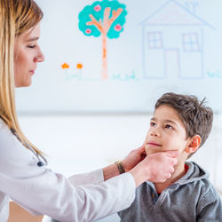 Female doctor pulling cheeks of boy at clinic