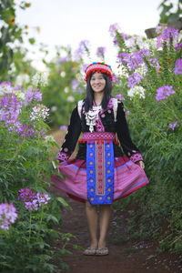 Portrait of a smiling young woman standing against purple flowering plants