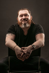 Portrait of man sitting against black background