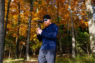 Bearded man photographing against trees during autumn