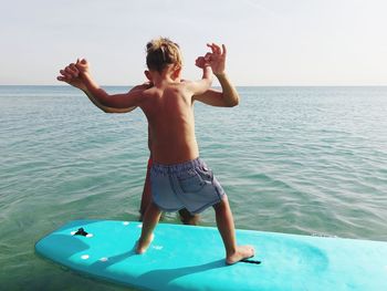 Rear view of woman with arms raised in sea against sky