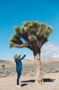 Full length of woman standing on palm tree against clear blue sky