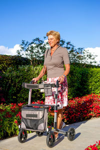 Senior woman with wheelchair walking by plants in park