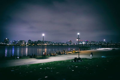 People on illuminated road by river in city