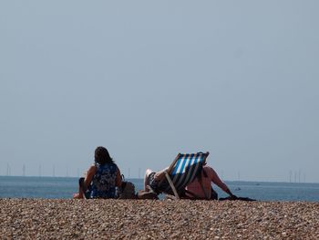People relaxing on beach against clear sky