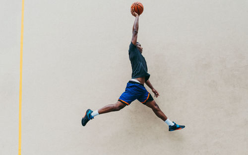 Young man playing basketball against wall