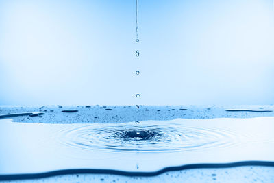 Close-up of drop falling on blue water against white background