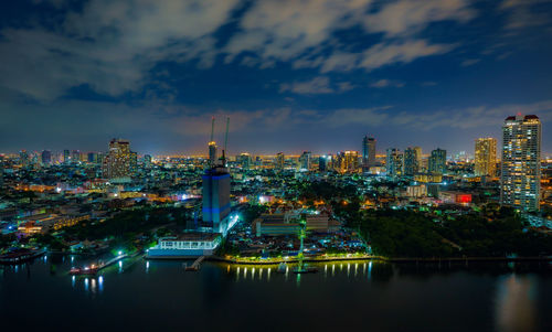 Illuminated buildings by river against sky at night