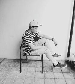 Side view of young man sitting on chair by wall