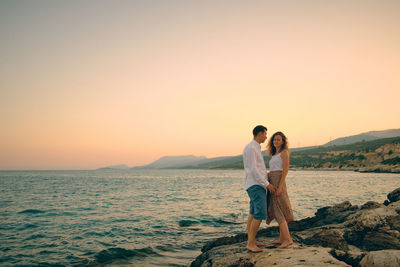 Romantic date on a sea coast. couple stands on sea rocks during sunset on an evening seaside date