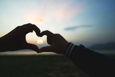 Close-up of hand holding heart shape against sky during sunset