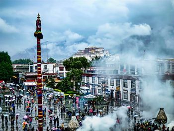 Panoramic view of crowd in city against cloudy sky