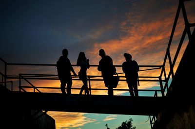 Low angle view of silhouette people standing on footbridge against sky during sunset