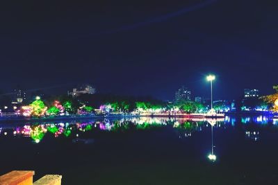 Illuminated city by river against clear sky at night