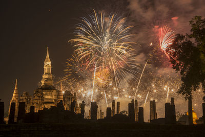 Firework display by illuminated buildings against sky at night