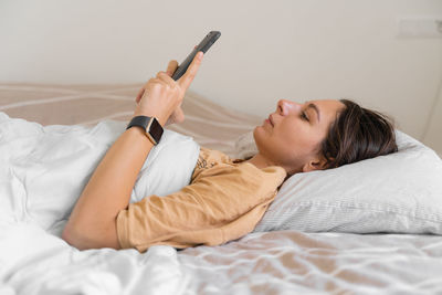 Young woman using mobile phone on bed at home