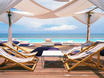 Deck chairs and tables at beach against sky